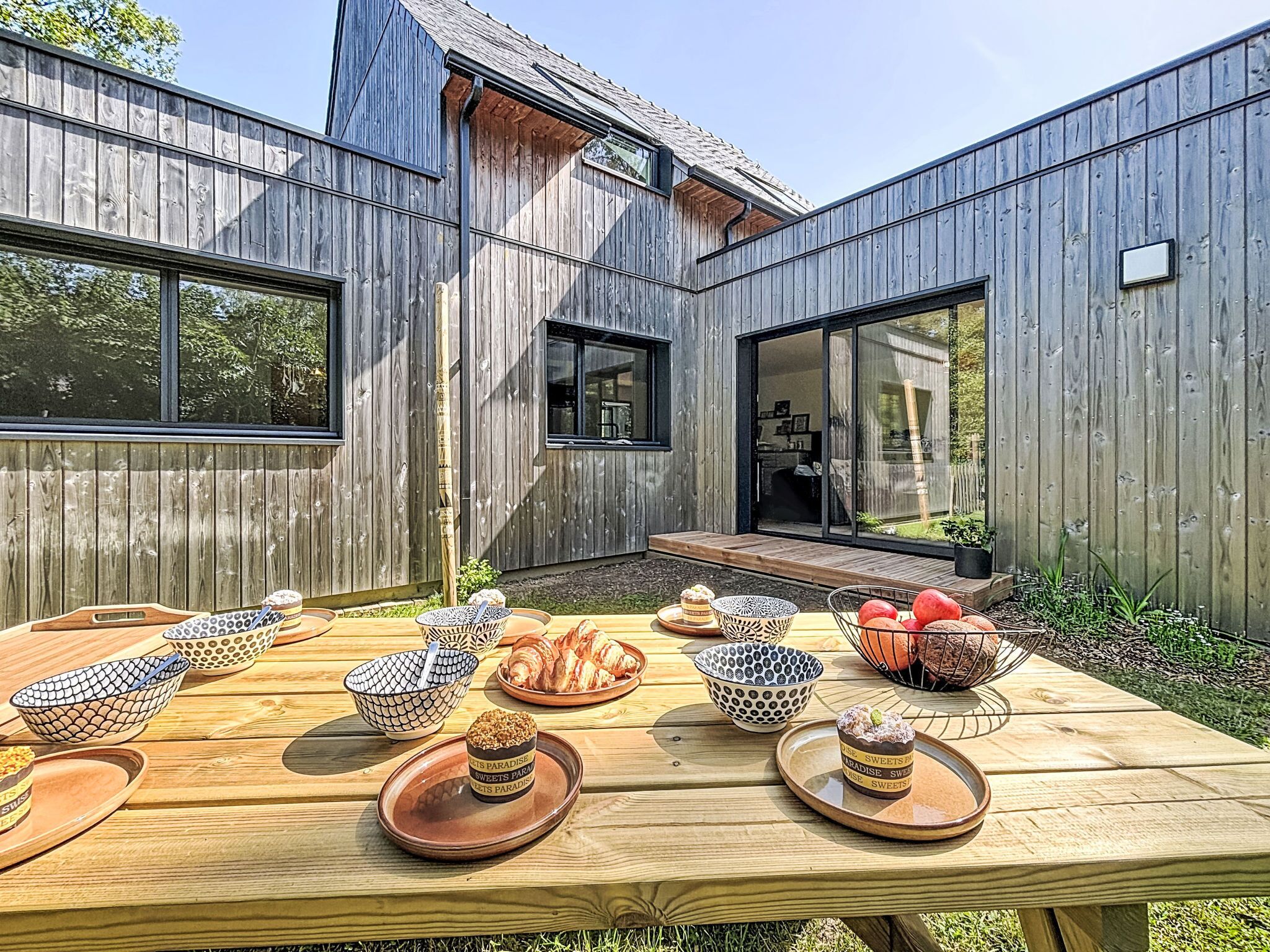 Una casa in legno con ampie finestre e un tavolo da patio con ciotole e dolci.