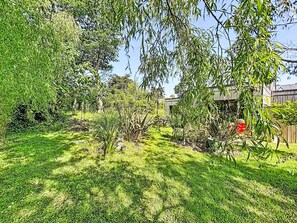 Un jardin luxuriant, avec une variété de plantes et d’arbres, une clôture en bois et un bâtiment en arrière-plan.