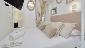 A hotel room with a bed, curtains, a mirror, and a TV mounted on the wall. - Apartment in Rome with 0 bedrooms sleeps 2 (Rome)