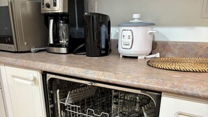 Et køkken med opvaskemaskine, kaffemaskine og riskoger på bordpladen.