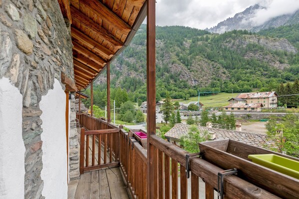 A balcony with a stone wall, wooden railing, and a view of a mountainous landscape.