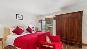 Un dormitorio con cama, almohadas rojas, un armario de madera y vistas a través de una ventana.