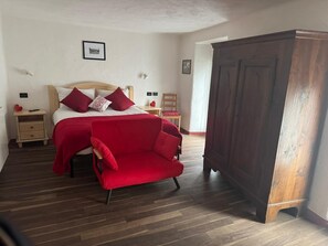 Una camera da letto con un letto, una sedia rossa, un armadio in legno e un comodino decorato con un cuore rosso.