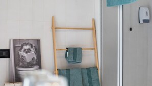 Un baño con un tendedero de madera, una toalla colgada en la pared y un dispensador de papel higiénico.