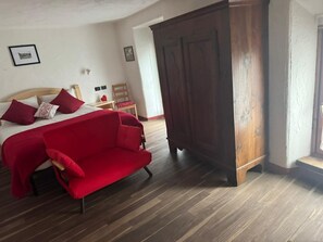 Una camera da letto con un letto, un divano rosso, un'armadiatura in legno e un pavimento di legno.