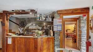 Un área de bar rústica con mostrador de madera, estantes con botellas y una pared de piedra.