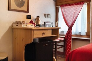 Habitación pequeña con escritorio de madera, refrigerador negro, una silla, cama, ventana con cortina roja y un cuadro en la pared.