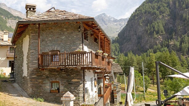 Ein Steinhaus mit einem hölzernen Balkon, einem kleinen Fenster und einer Treppe zum Eingang.