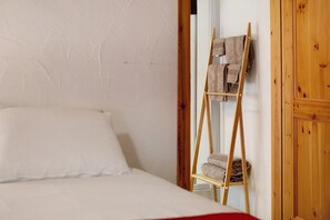 Un lit avec une literie blanche, une échelle en bois appuyée contre un mur et une porte en bois.