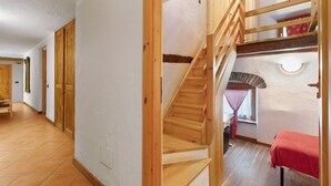 Eine Holztreppe führt zu einer oberen Ebene, ein rotes Bett und ein Fenster mit Vorhang.
