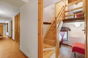 Una escalera de madera que lleva a un nivel superior, una cama roja y una ventana con cortina.