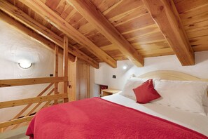 Un plafond en bois, un lit avec une literie blanche et un oreiller rouge, et un escalier en bois.