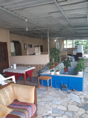 A covered outdoor seating area with a table, chairs, a sofa, and potted plants.