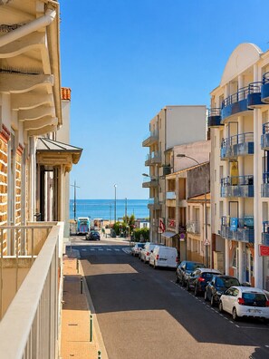 Eine Küstenstraße mit parkenden Autos, Gebäuden mit Balkonen und freiem Blick auf das Meer.