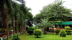 A well-maintained garden with various trees and shrubs, a pathway, and a building with a green roof. - Wayanad Cave N Pillar Resort (Krishnagiri)