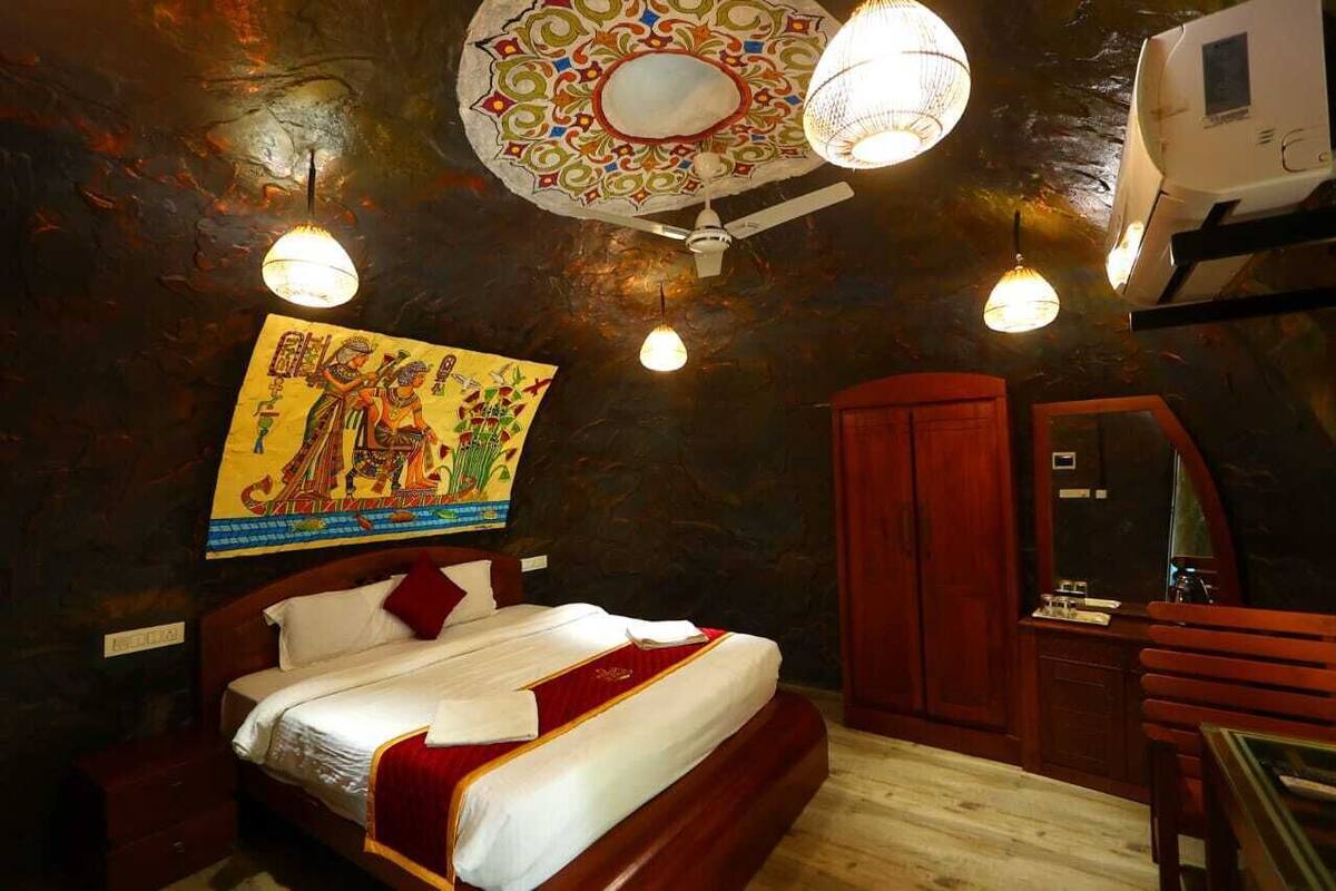 A bedroom with a bed, a wooden wardrobe, a mirror, and a wall with a colorful painting.
