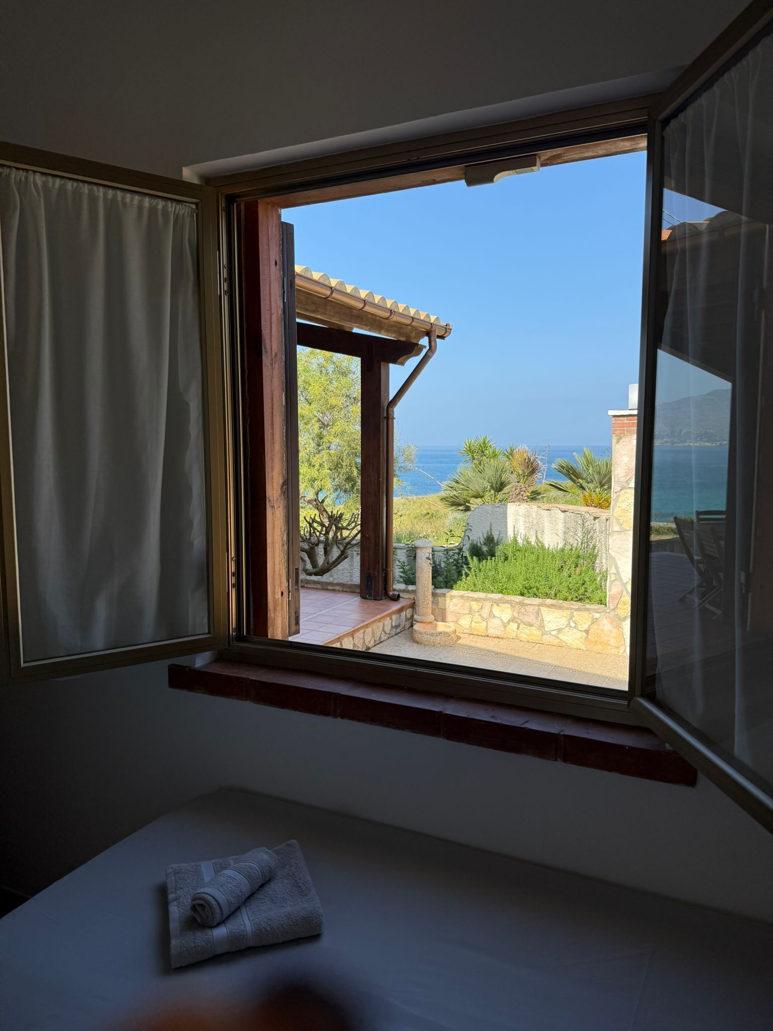 A room with a window overlooking a patio with a view of the sea.