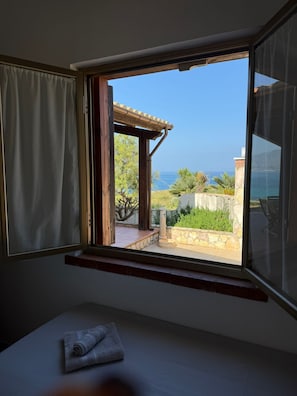 A room with a window overlooking a patio with a view of the sea.