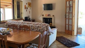 Un comedor con mesa y sillas de madera, televisor montado en la pared y chimenea.