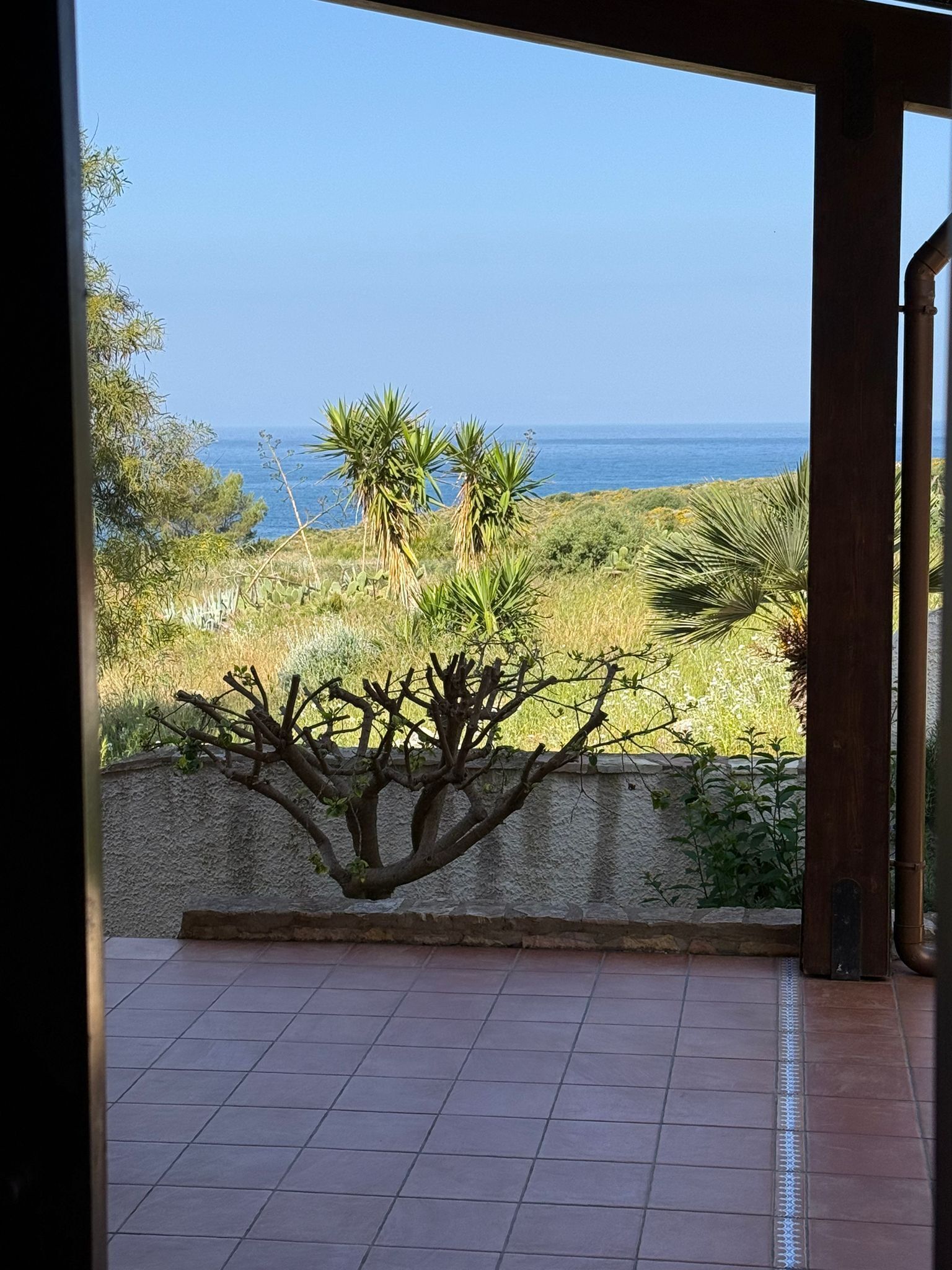 A view from a room with a tiled floor and a view of the ocean and vegetation outside.