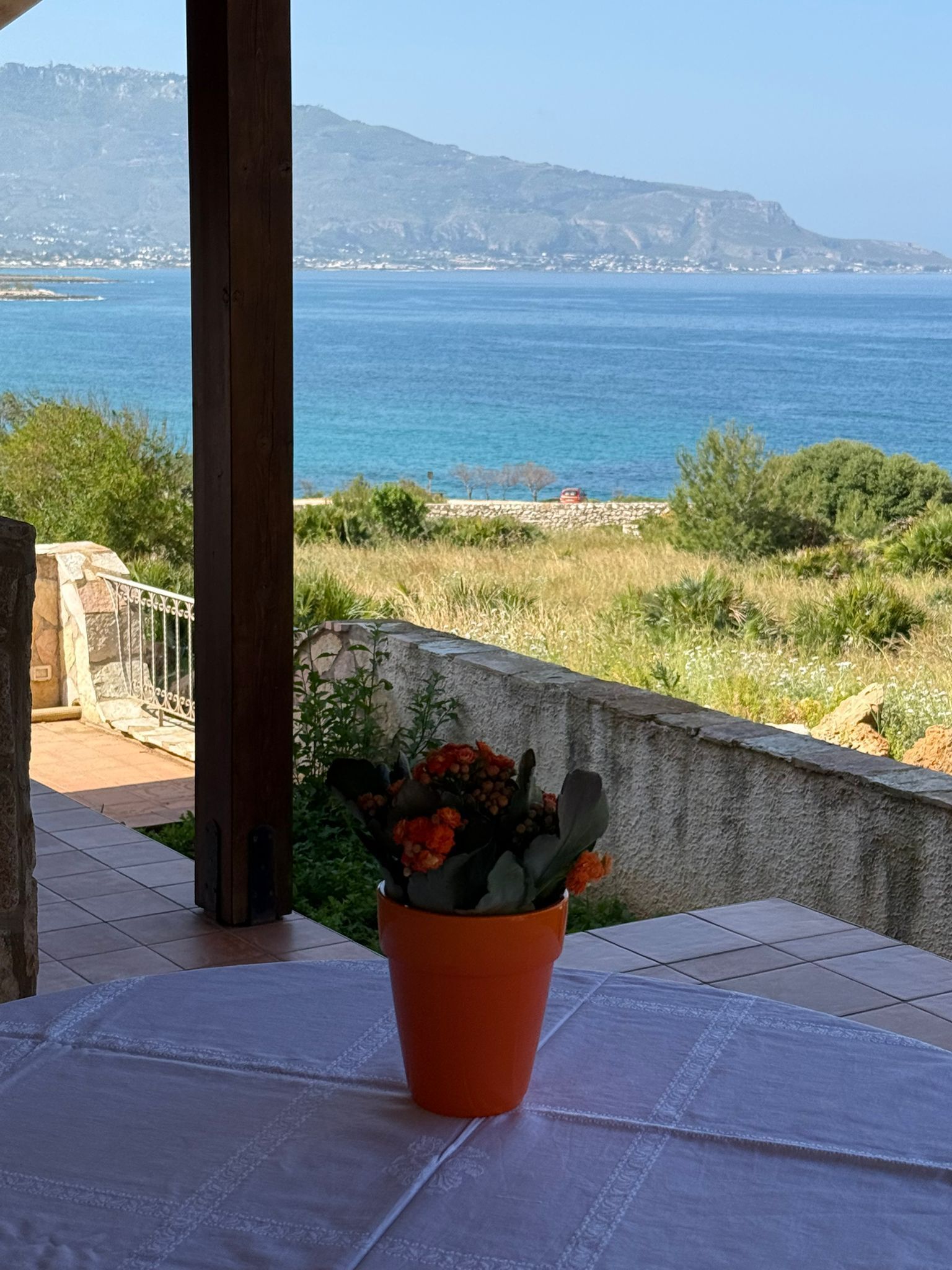 Een terras met een bloempot, een tafel en uitzicht op zee en het verre land.