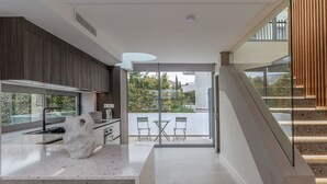 A modern kitchen with a large island, a dining area with a glass door leading to a balcony, and a staircase. - Sea View Riviera Maisonette with Large Terraces (Voula)