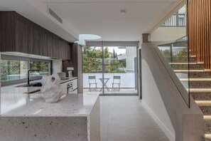 Eine moderne Küche mit einer großen Kochinsel, einem Essbereich mit Glastür zum Balkon und einer Treppe.