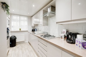 A modern kitchen with white cabinets, a gas stove, a coffee machine, and a window with blinds.