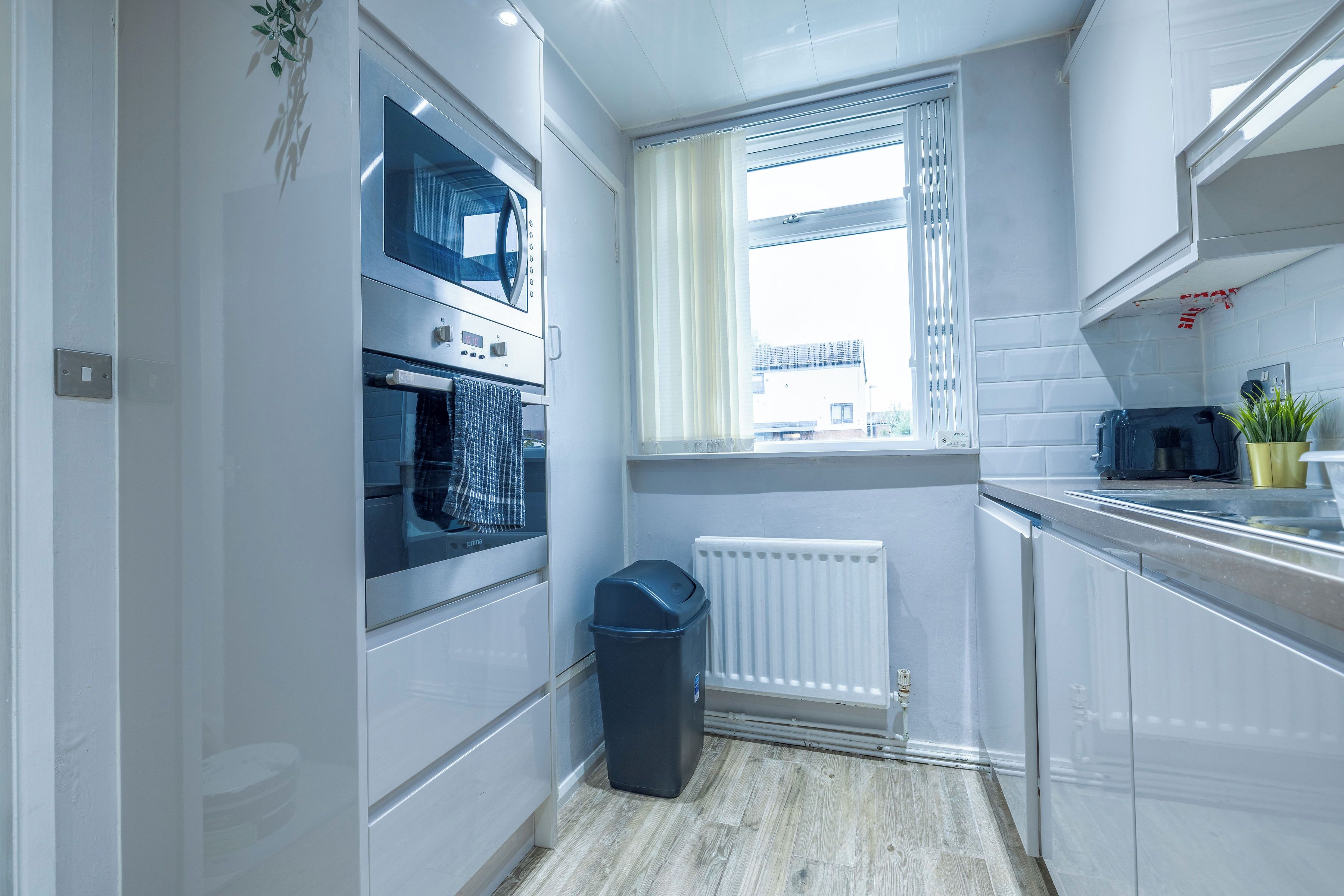 A modern kitchen with built-in appliances, a window with blinds, and a radiator.