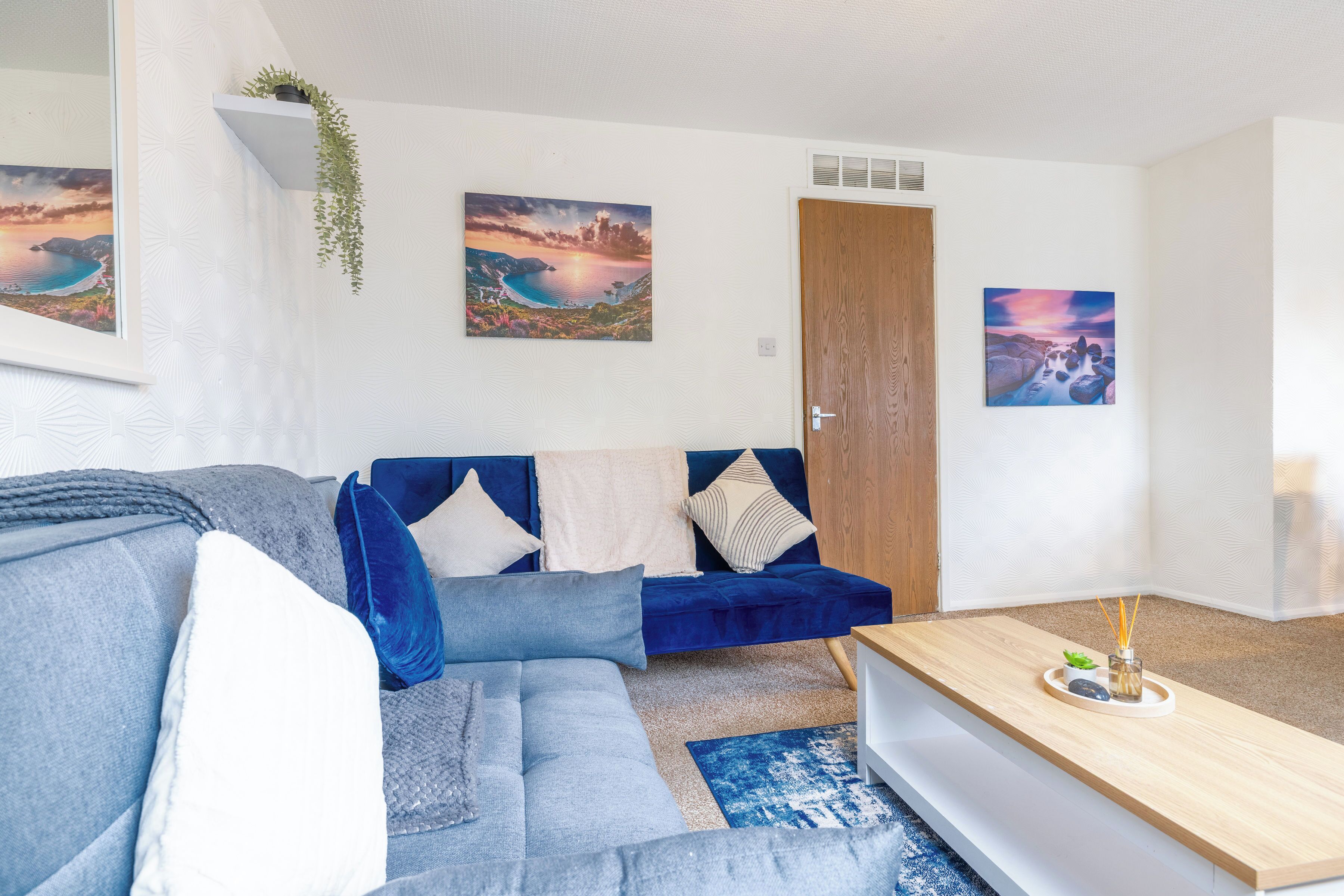 A modern living room with a blue sofa, a wooden coffee table, and two framed landscape paintings.