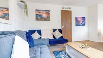 A modern living room with a blue sofa, a wooden coffee table, and two framed landscape paintings.