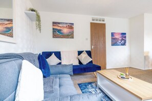 A modern living room with a blue sofa, a wooden coffee table, and two framed landscape paintings.