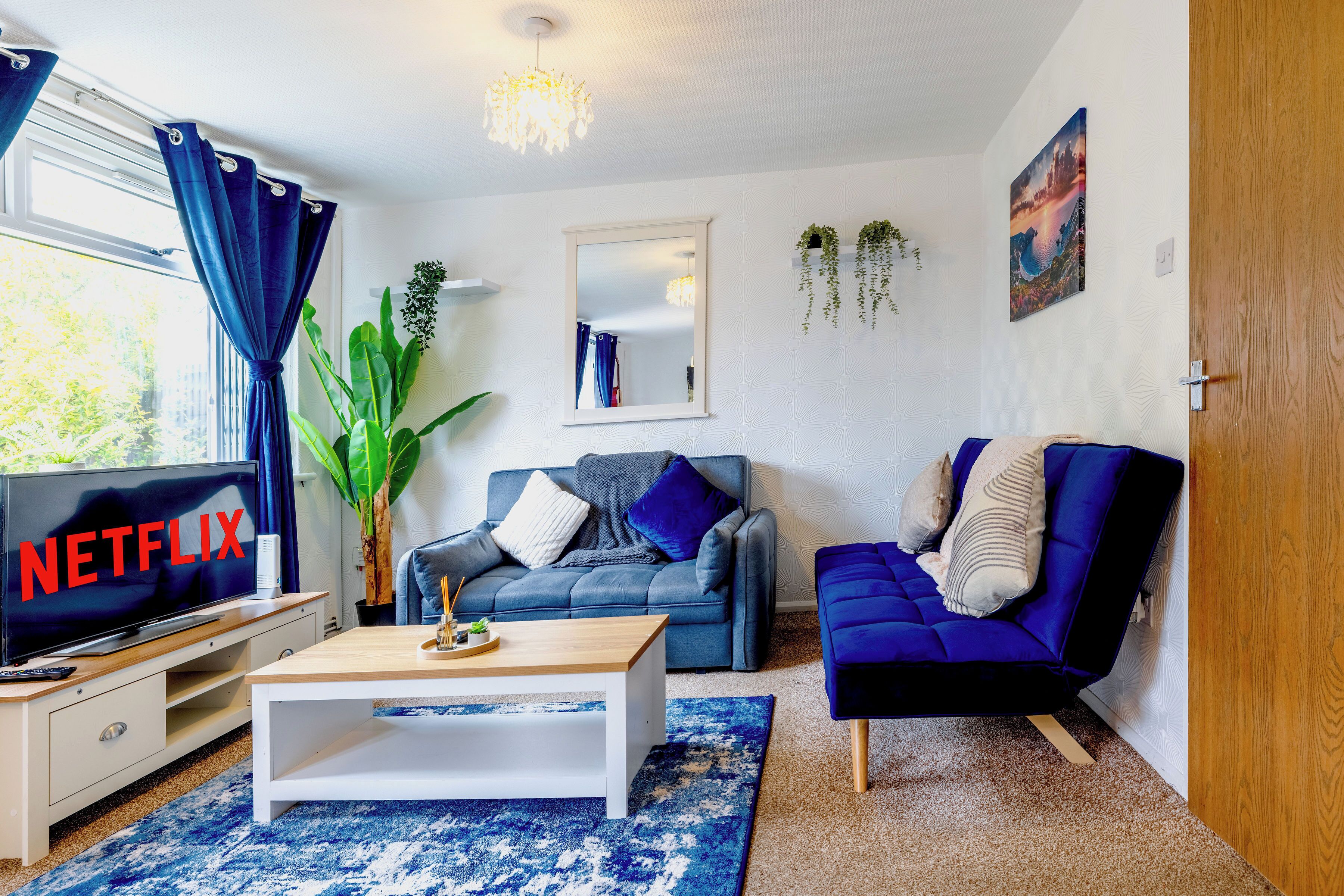 A living room with a TV displaying 'NETFLIX', a sofa, a chair, a coffee table, and a large plant.