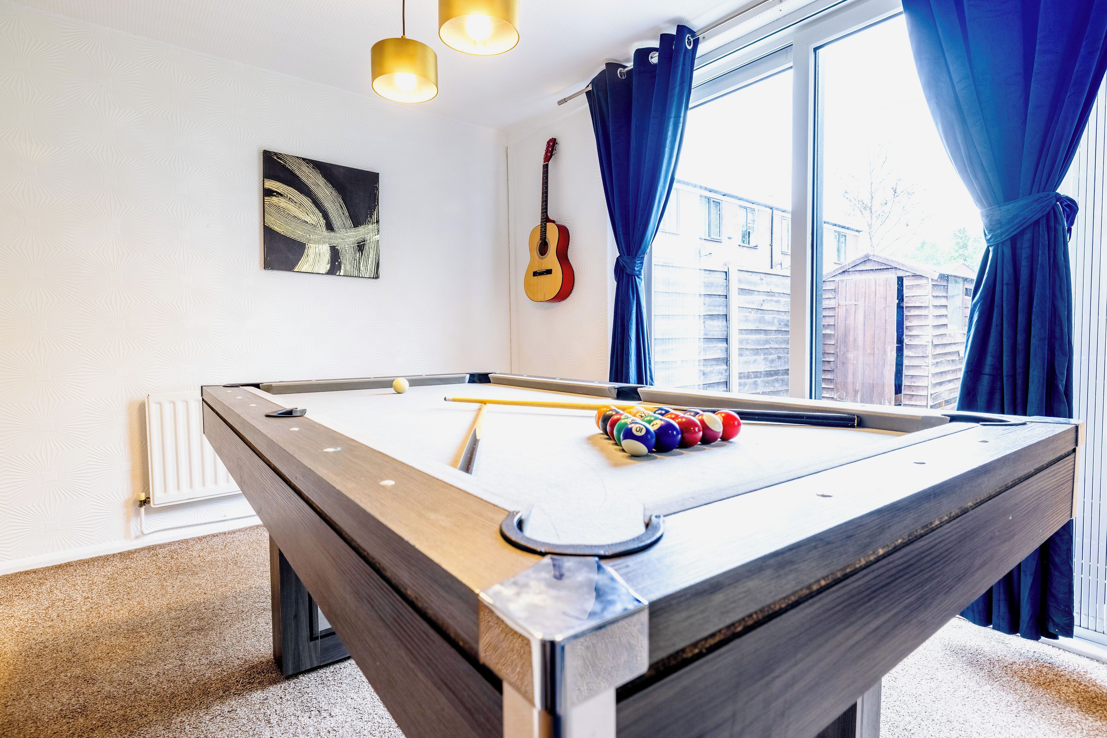 Uma mesa de bilhar com bolas, uma guitarra e um quadro na parede.