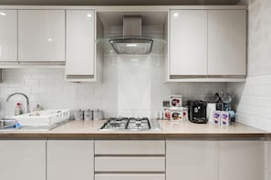 Une cuisine moderne avec des meubles blancs, une cuisiniÚre à gaz, une machine à café et un égouttoir à vaisselle.
