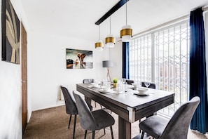 A dining area with a dark wooden table, grey upholstered chairs, and pendant lights.