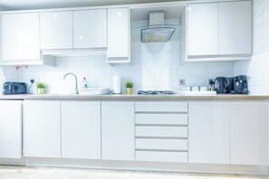 Una cocina moderna con gabinetes blancos, una campana extractora de acero inoxidable, un lavamanos integrado y una cafetera.