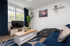 A modern living room with a television, a sofa, a coffee table, and a large window with curtains.