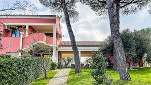 A red building with a paved pathway leading to a covered area, surrounded by trees and greenery. - Vacation home Vidal by Interhome (Spoltore)