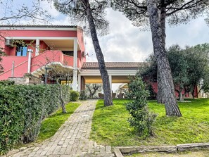 A red building with a paved pathway leading to a covered area, surrounded by trees and greenery. - Vacation home Vidal by Interhome (Spoltore)
