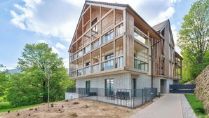 A multi-story building with a wooden facade, large windows, and a paved entrance area. - Comfortable Apartment with a Balcony | Parking (Karpacz)