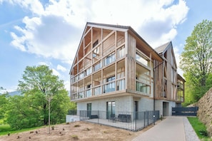 Un immeuble à plusieurs étages doté d’une façade en bois, de grandes fenêtres et d’un espace d’entrée pavé.