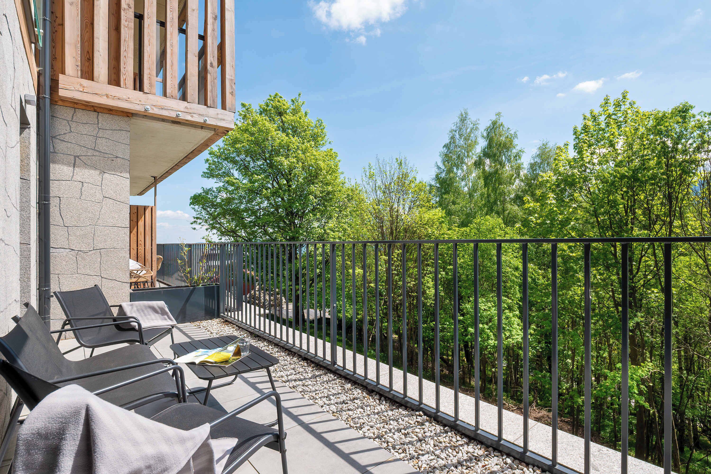 Un balcon aménagé avec du mobilier d’extérieur, un mur en pierre et une vue sur une forêt.