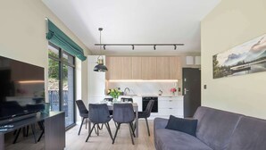 A modern living space with a flat-screen TV, a sofa, a dining area with chairs, and a kitchen with wooden cabinets. - Comfortable Apartment with a Balcony | Parking (Karpacz)