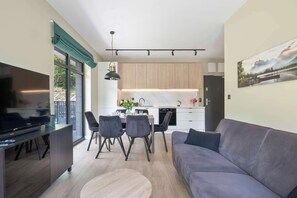 A modern living room with a flat-screen TV, a grey sofa, and a dining area with a table and chairs. - Air Conditioned Apartment with Balcony | Parking (Karpacz)