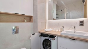 A modern bathroom with a built-in washing machine, a large mirror, and a wooden countertop. - Comfortable Apartment with a Balcony | Parking (Karpacz)