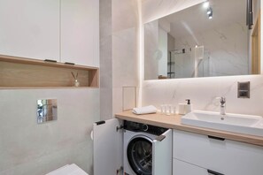 A modern bathroom with a built-in washing machine, a large mirror, and a wooden countertop. - Air Conditioned Apartment with Balcony | Parking (Karpacz)