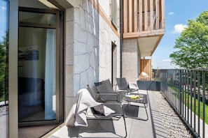Un espace extérieur moderne aménagé avec des chaises et une table, une entrée avec une porte vitrée et un balcon doté de rampes en bois.