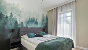 A bedroom with a bed, nightstand, and a forest mural on the wall. - Comfortable Apartment with a Balcony | Parking (Karpacz)