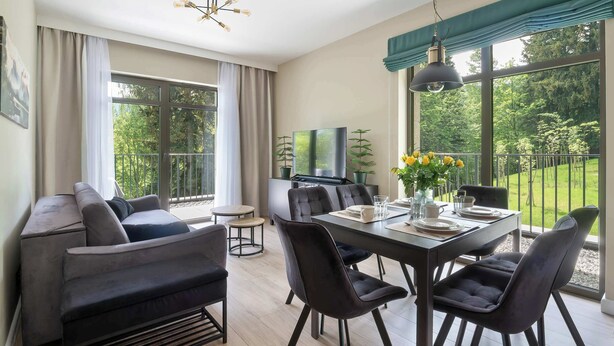 A modern living room with a sofa, dining table, chairs, and a TV. - Comfortable Apartment with a Balcony | Parking (Karpacz)